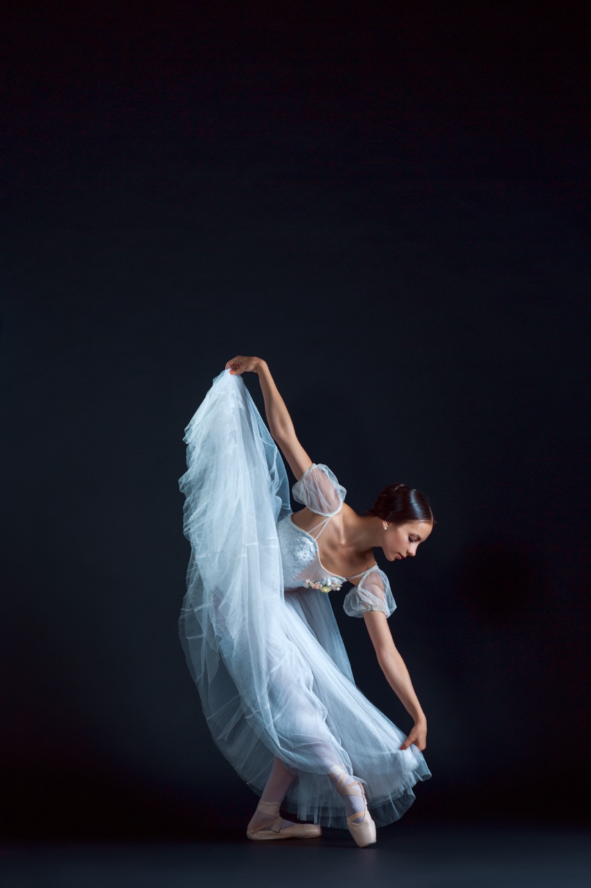 Portrait of the classical ballerina in white dress on black background