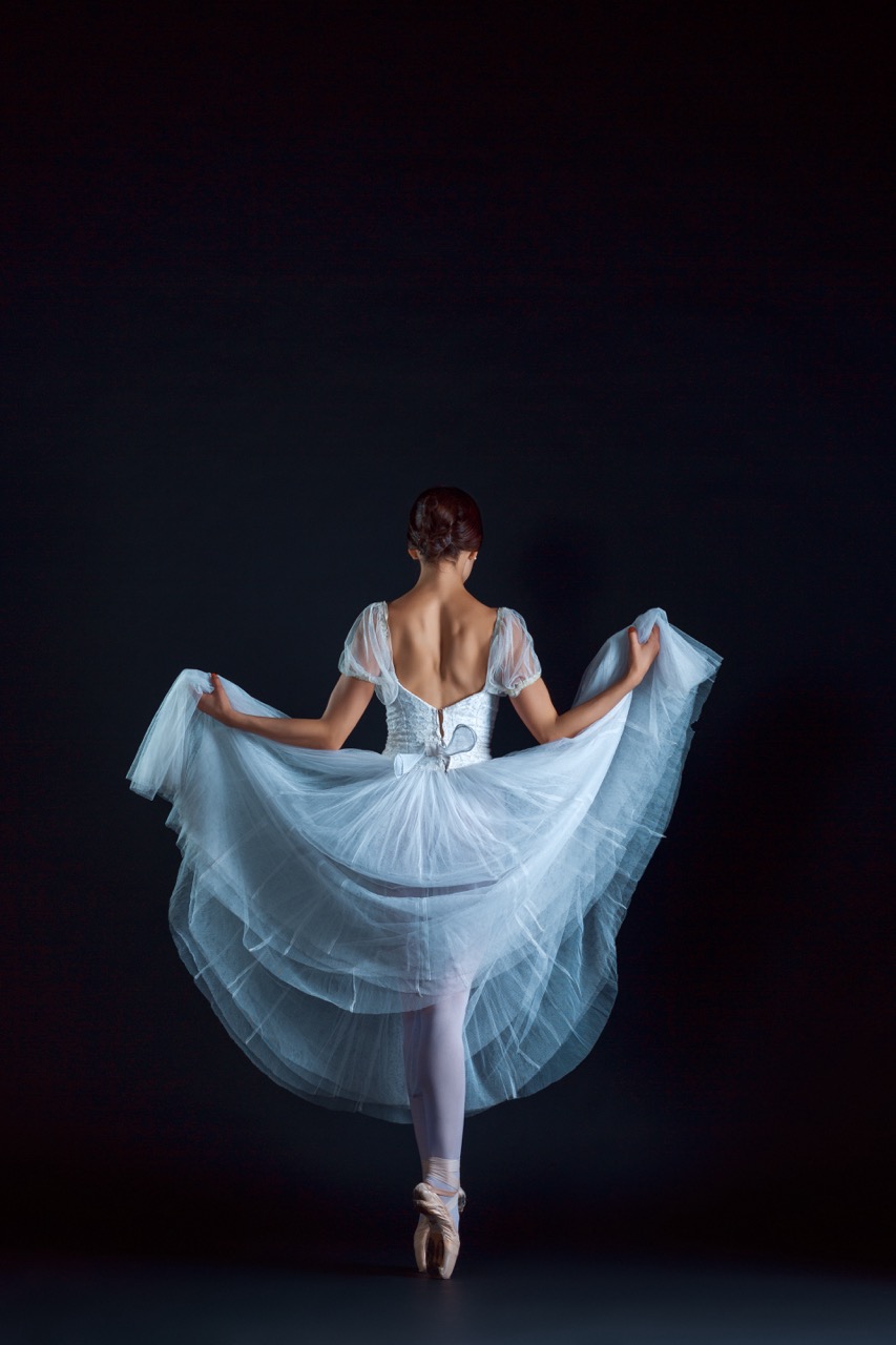 Portrait of the classical ballerina in white dress on black background