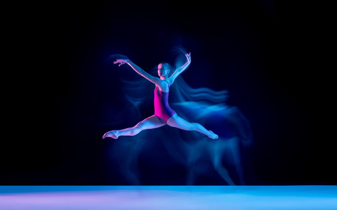Young and graceful ballet dancer isolated on purple studio background in neon light