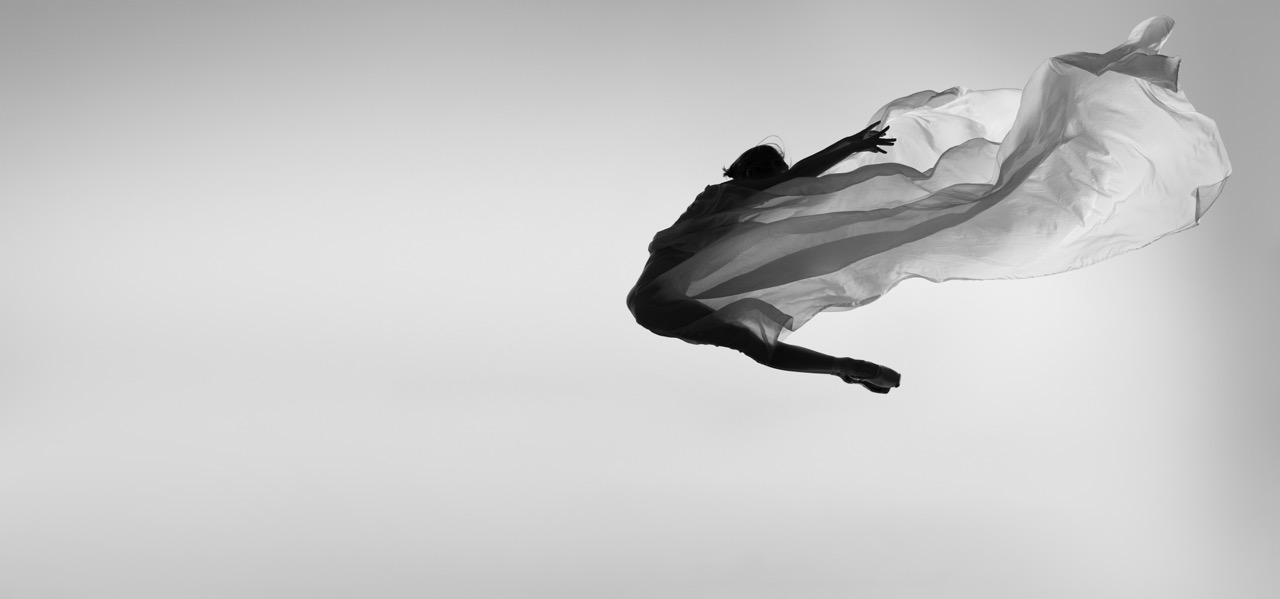 Flying high. Professional ballering dancing with transparent veil, making movements in a jump. Black and white